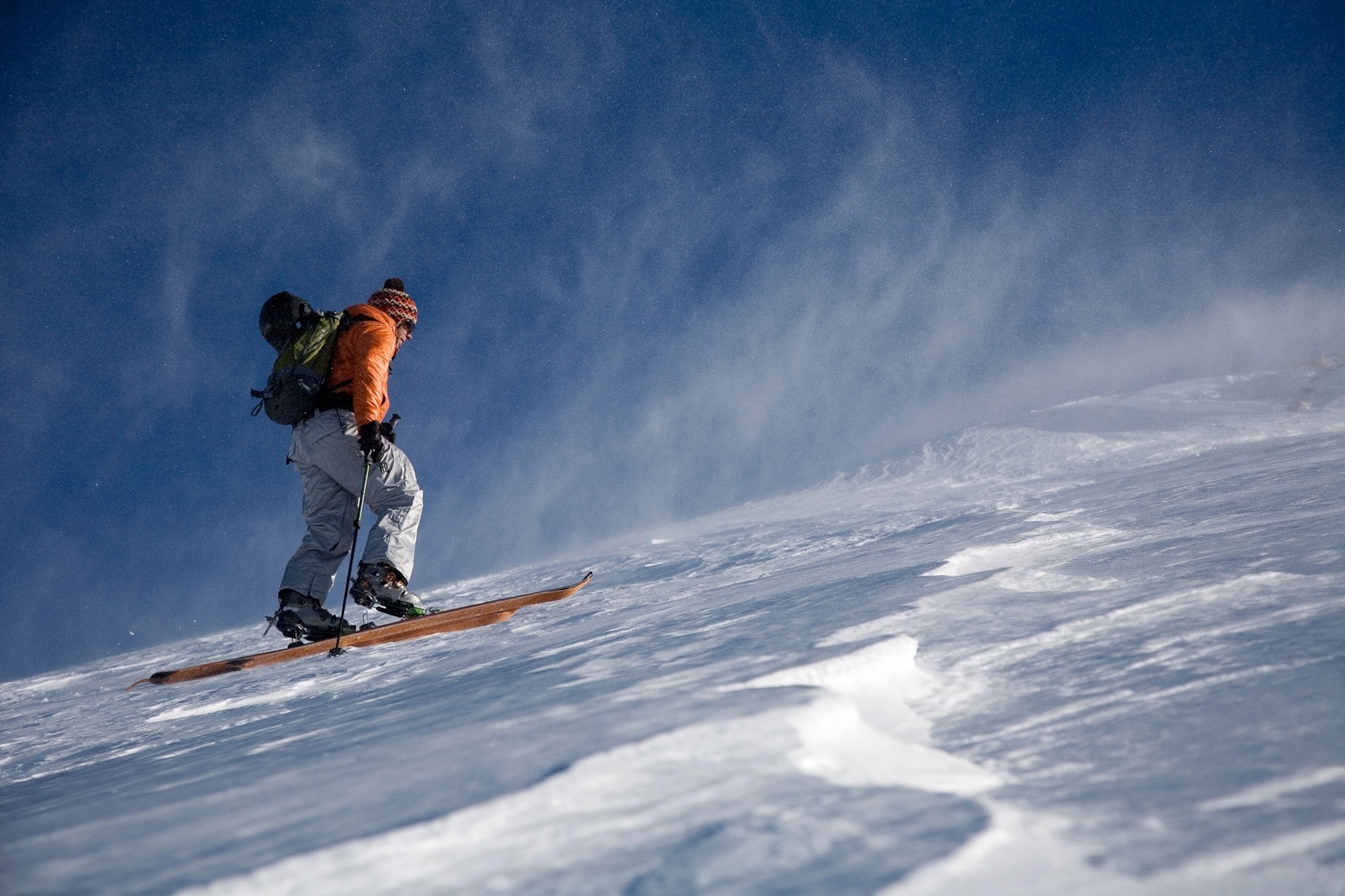 A man in light ski pants and orange ski jacket with skis and ski poles on a snow covered inclined