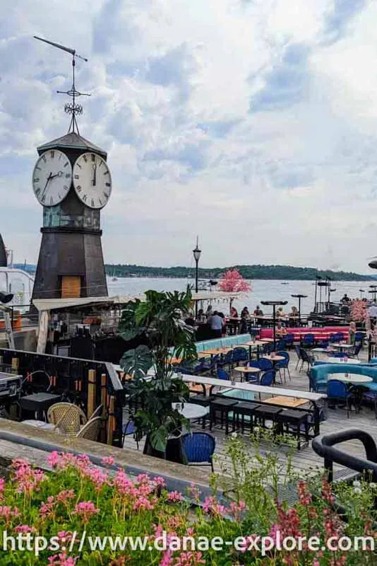 Cafés by the fjord in Oslo. A tower with a clock is visible.
