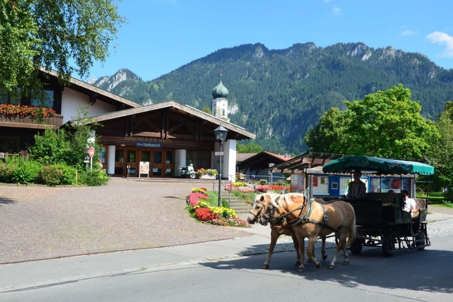 A carriage, pulled by two light-brown horses, drives in front of Oberammergau