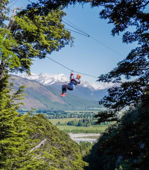 Person ziplining with snow-covered mountain in the back
