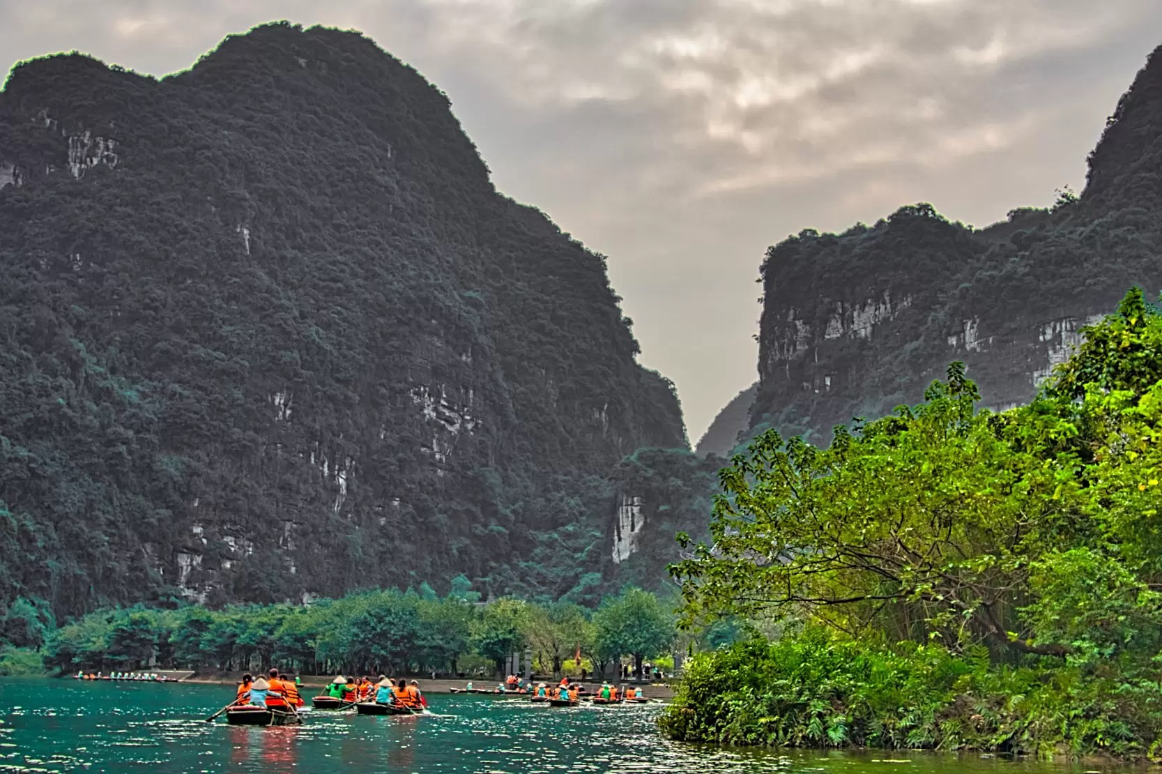 Tall mountains rise above the Trang An River and its many boats in Vietnam