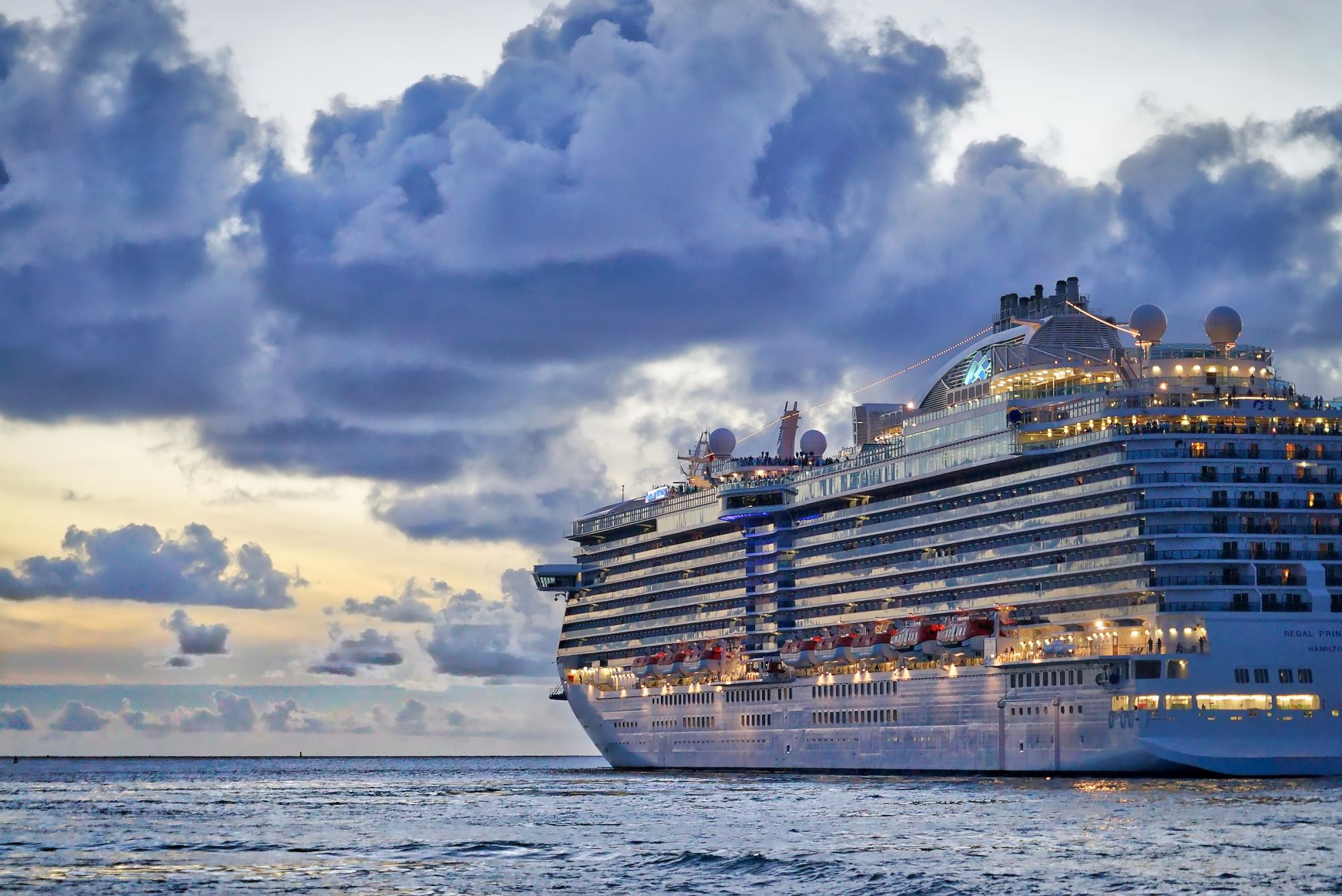 A cruise ship lit up at dusk sailing away from an island