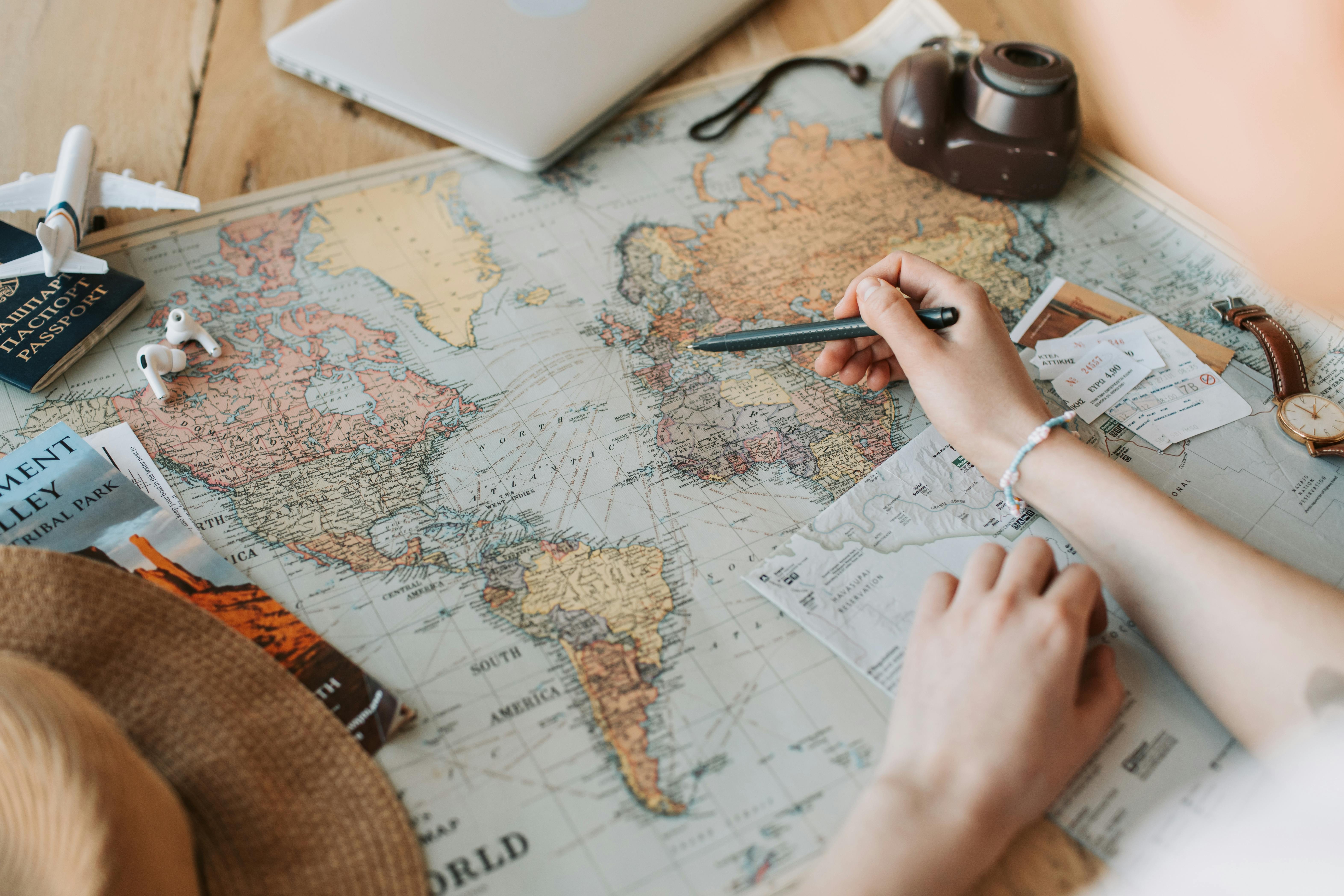 A person planning a trip with a world map, travel tickets, and a pencil, surrounded by a hat, passport, camera, and small airplane model.