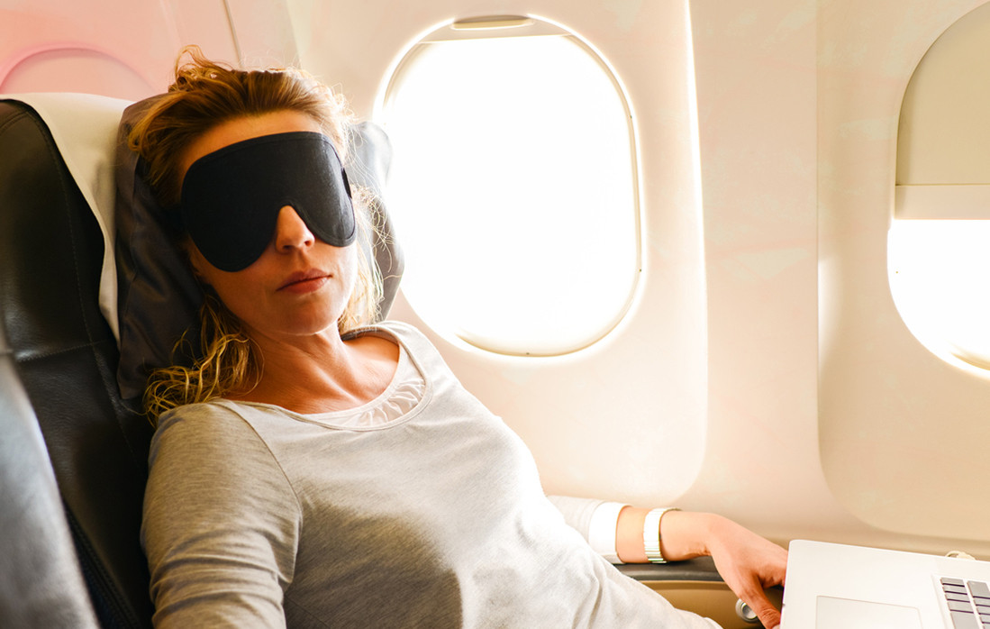 Woman sleeping comfortably on a plane with a neck pillow, showcasing the comfort and relaxation a travel pillow can provide
