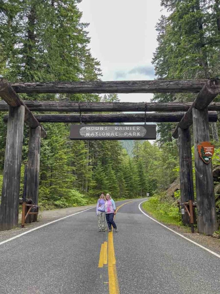 Two individuals stand under a large wooden archway with a sign reading 