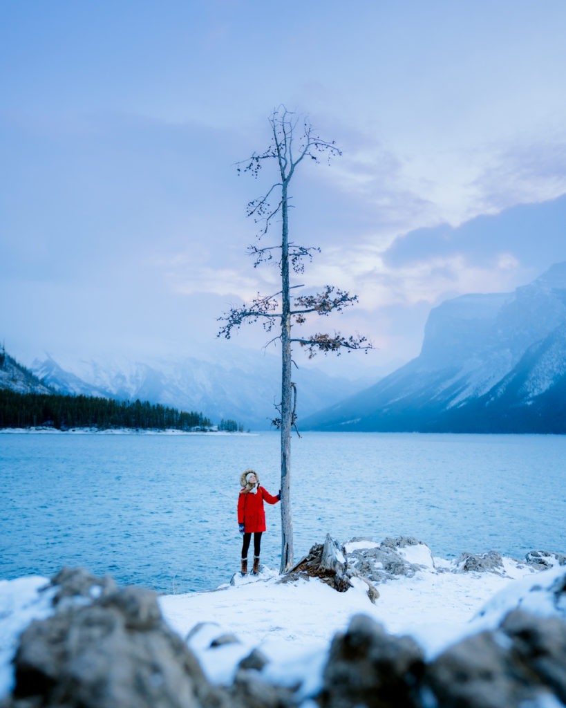 Lake Minnewanka in Winter, Banff National Park, Canada. The lake is partially frozen and surrounded by snow-covered mountains, showcasing the serene beauty of Banff winter tourism.