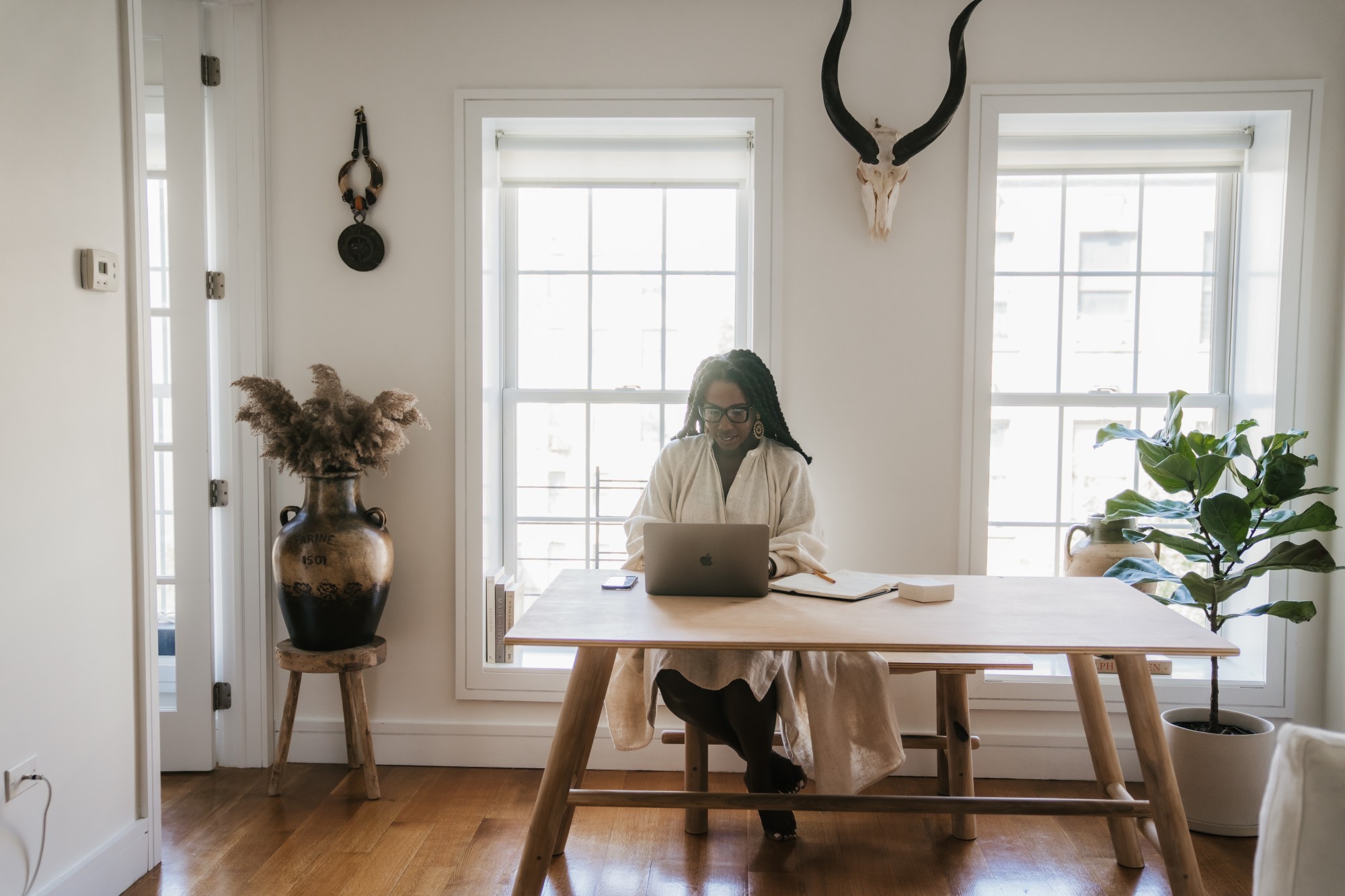 Woman in white dress working on her laptop while sitting at a wooden table