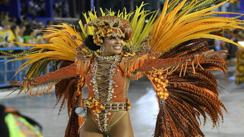 A dancer in vibrant carnival costume with elaborate headdress and feathered wings at a parade, celebrating sustainable tourism in Latin America.