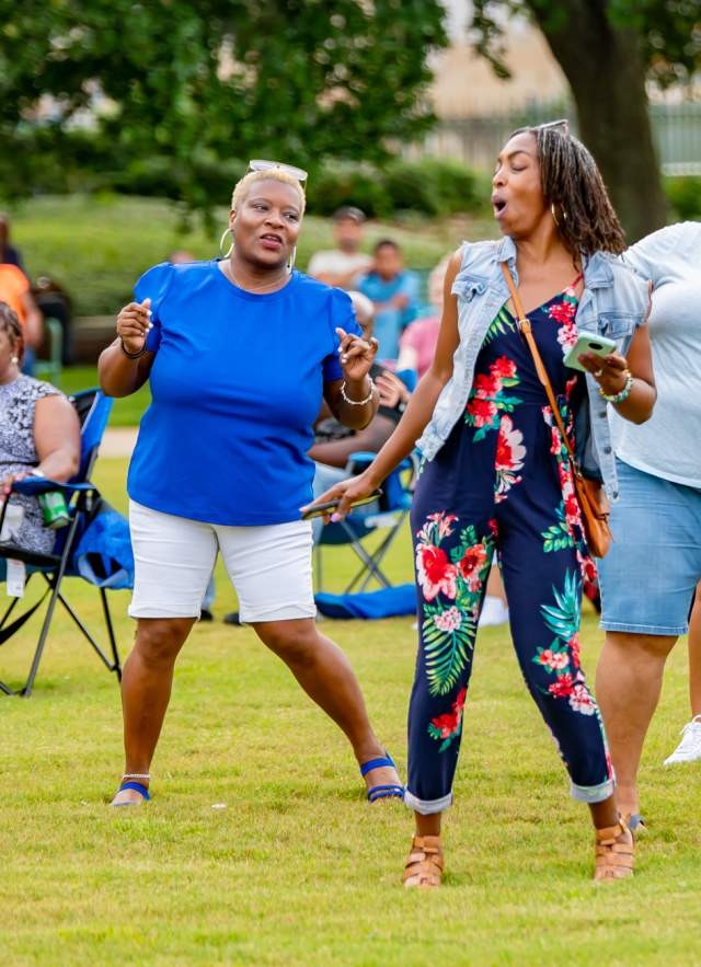 Four people dancing in a park as a band plays, creating a joyful atmosphere