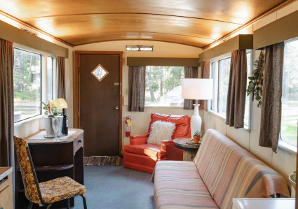People gathered around a vintage travel trailer at a campsite, enjoying a social gathering with food, drinks, and music