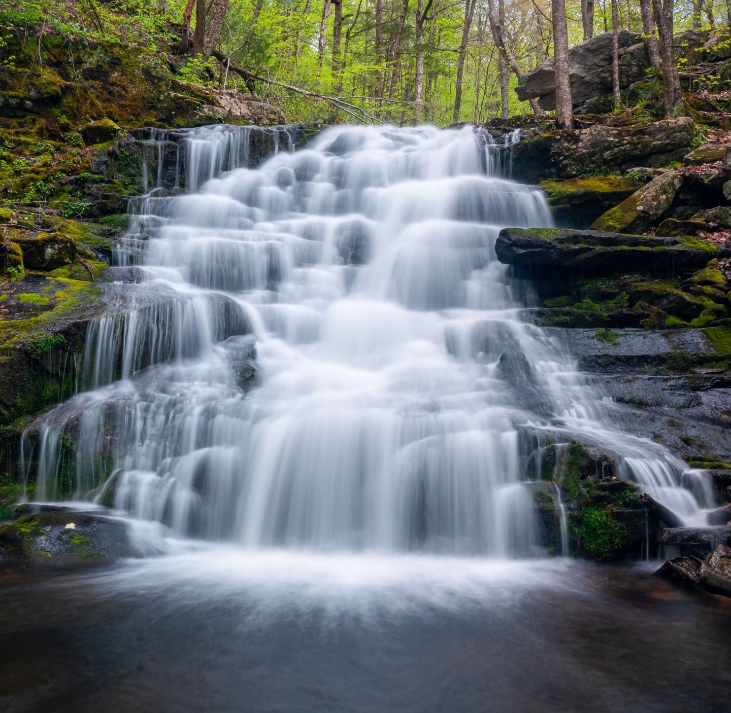 a lesser known waterfall in connecticut in summer surrounded by green leaves