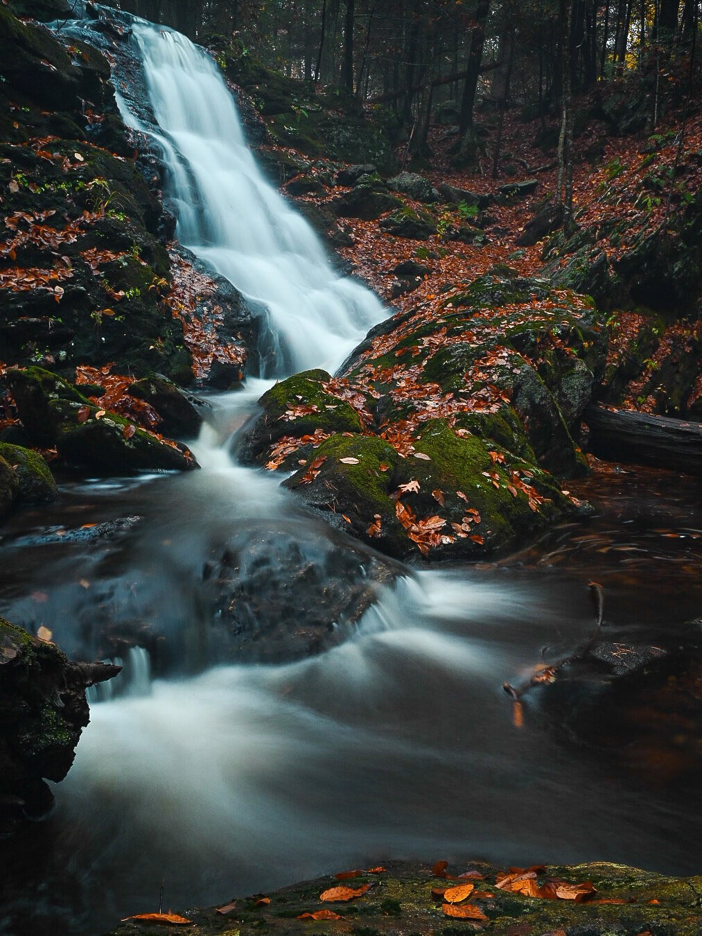 a lesser known and secluded waterfall in connecticut in the fall surrounded by orange and red leaves