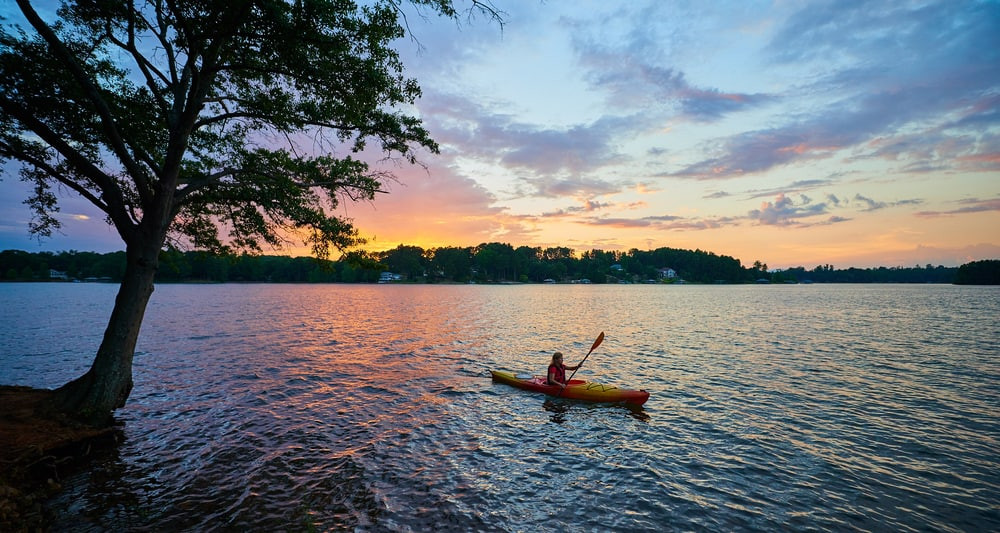 A picturesque view of Seneca, South Carolina, featuring a calm lake surrounded by lush green trees and a clear blue sky