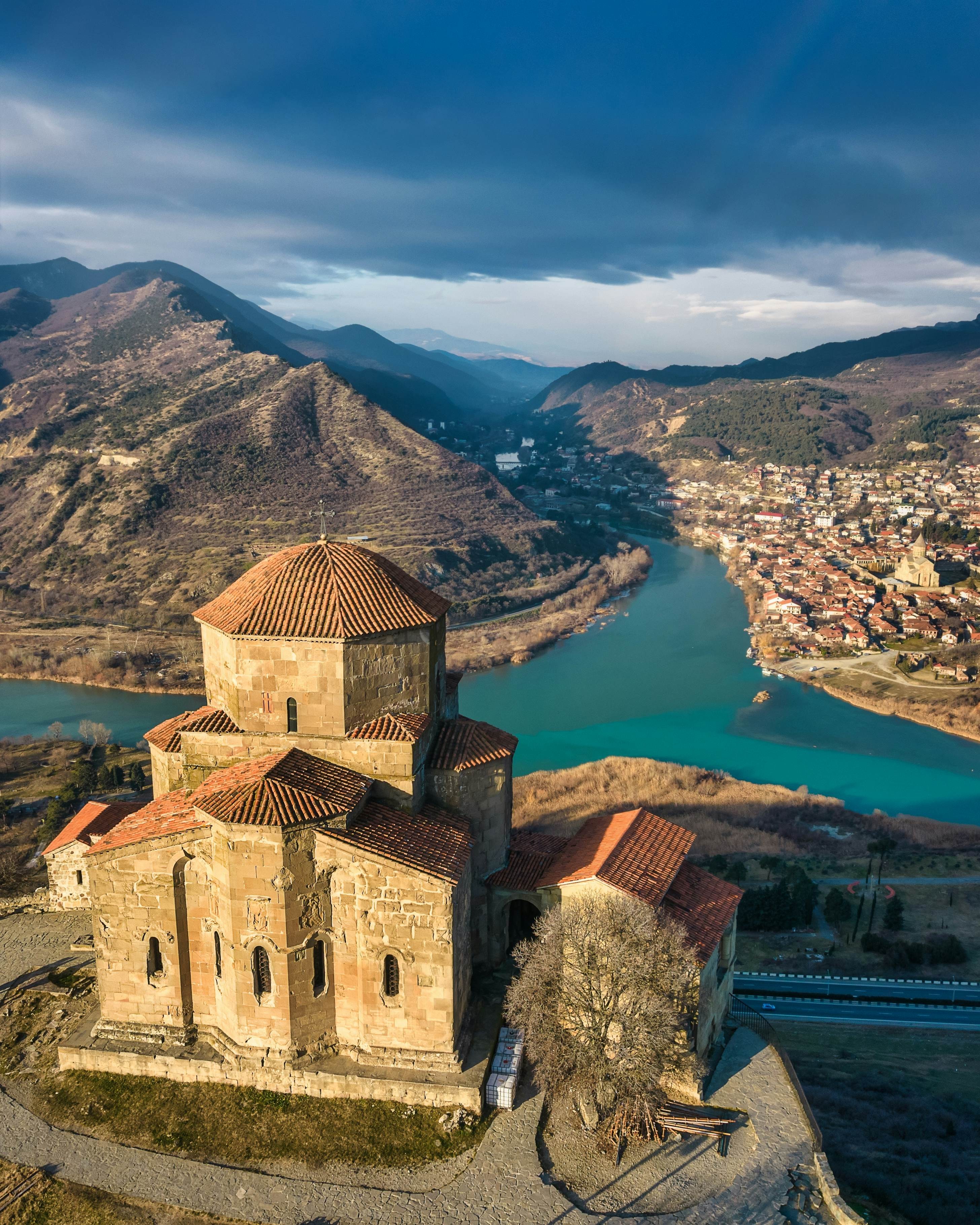 An ancient monastery stands on a hilltop; two rivers meet in the valley below, and there