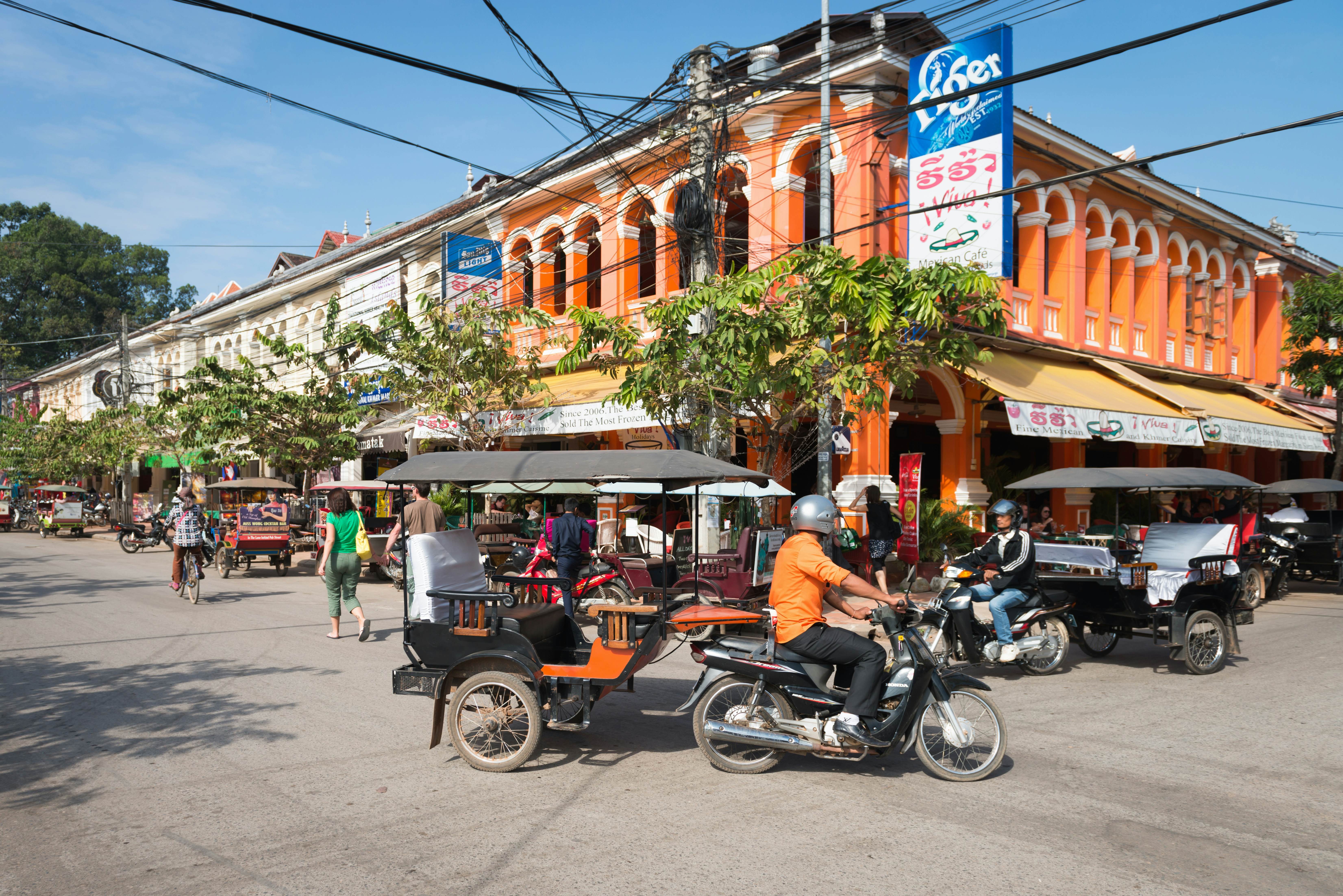Tuk-tuk tourist taxi on the central street of Siem Reap with colonial architecture buildings