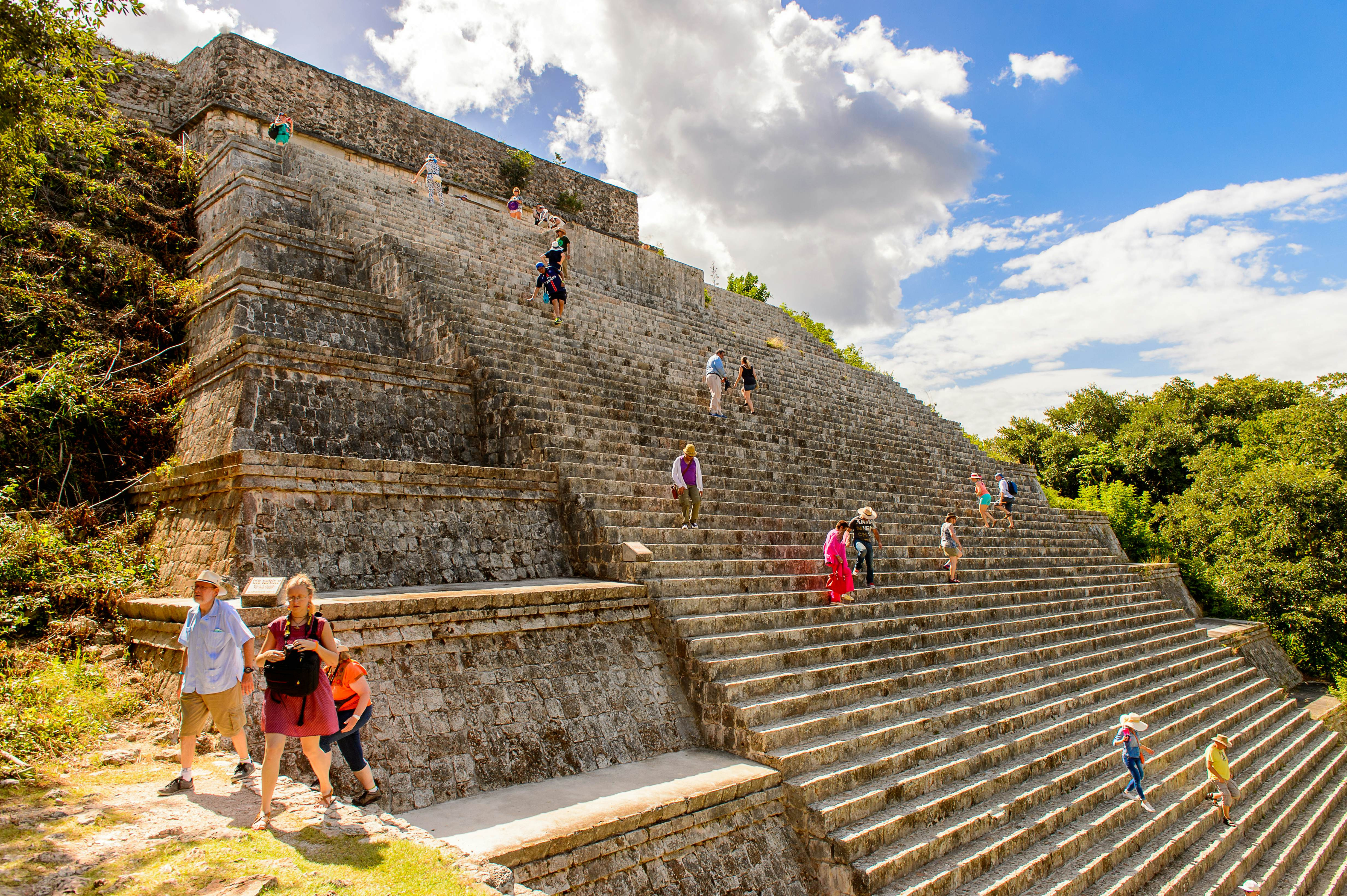 People climb the steeps steps of an ancient pyramid at an archeological site.