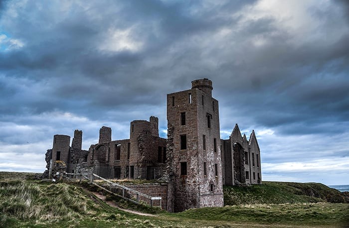 The picturesque yet haunting ruins of New Slains Castle, perched on a cliff overlooking the stormy North Sea, providing an evocative experience for dark tourism enthusiasts.