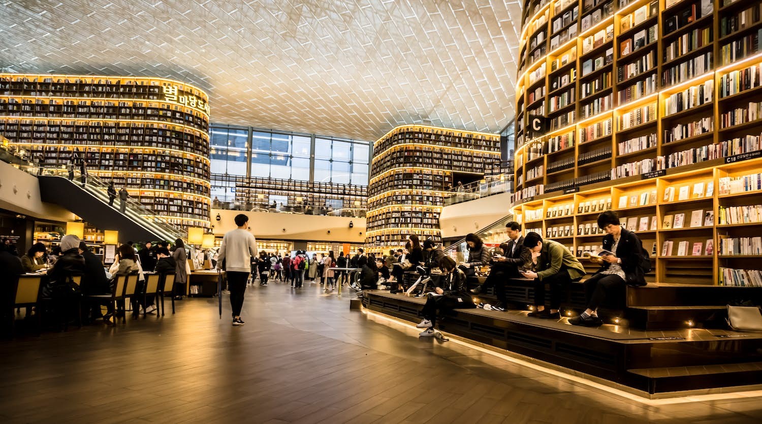 A vast library space with floor-to-ceiling book shelves and many places for people to sit and read