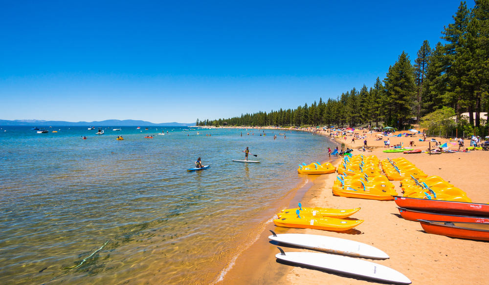 A stunning panoramic view of South Lake Tahoe, California, featuring the crystal-clear lake surrounded by towering pine trees and snow-capped mountains