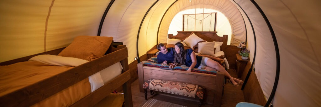 Couple relaxing on a bed in a covered wagon at Splash RV Resort near Navarre Beach, Florida