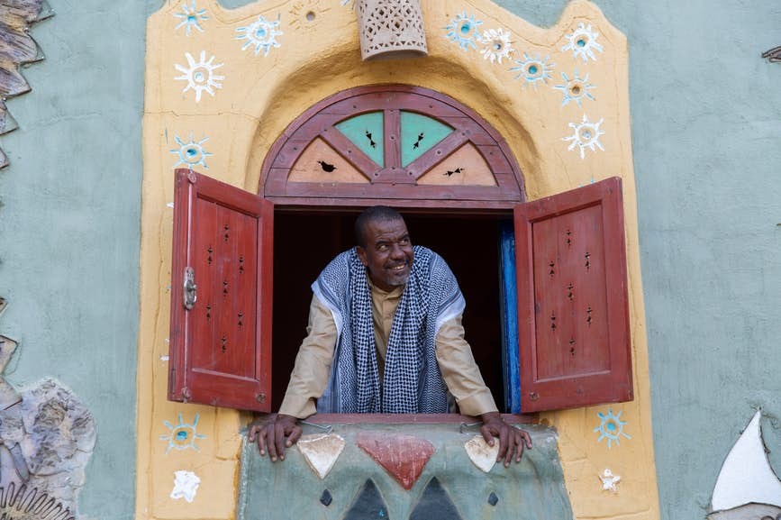 Nubian restaurant owner in traditional Galabeya dress peering out of window in rural Nubian Village, Aswan Egypt