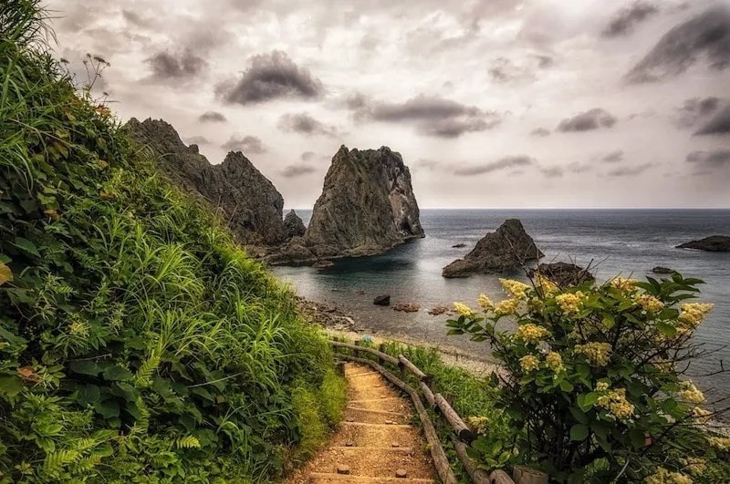 A tourist traveling in the Japanese countryside walks along a seaside path in rural Hokkaido
