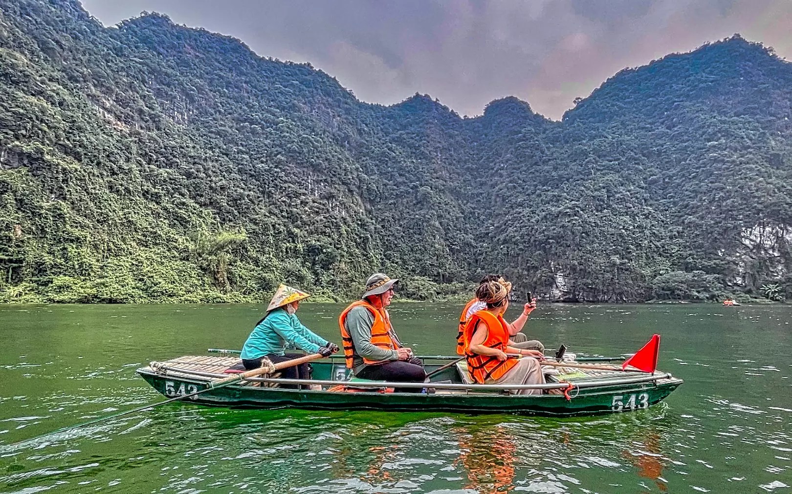 Older man sitting on a boat between the rower and a young couple on the Trang An River
