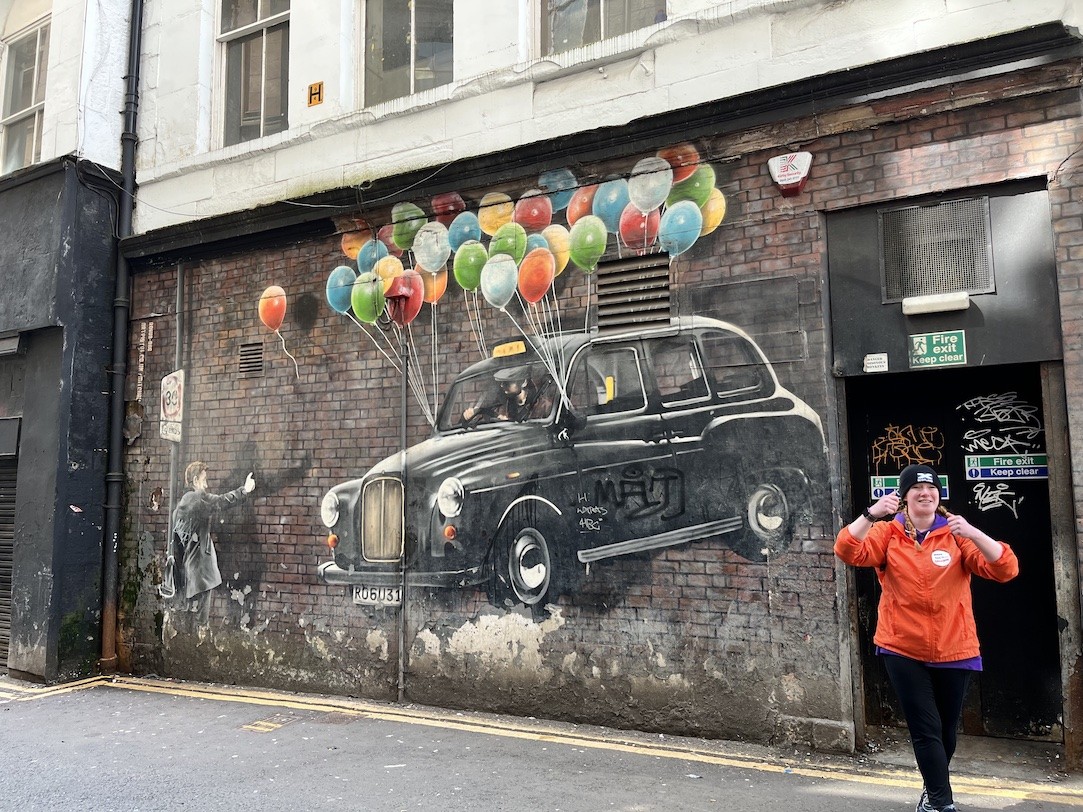 A tour guide smiles and points at a graffiti piece