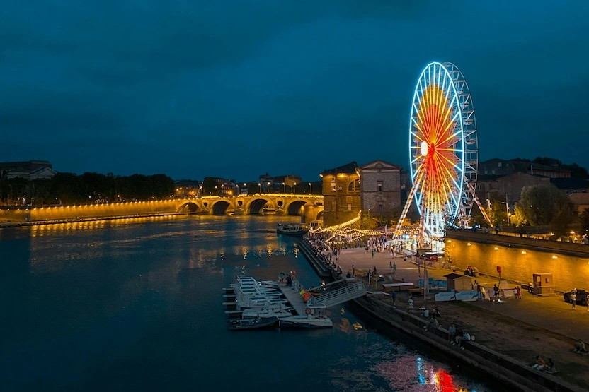 A lit up ferris wheel on the Garonne River in Toulouse, France at night. 