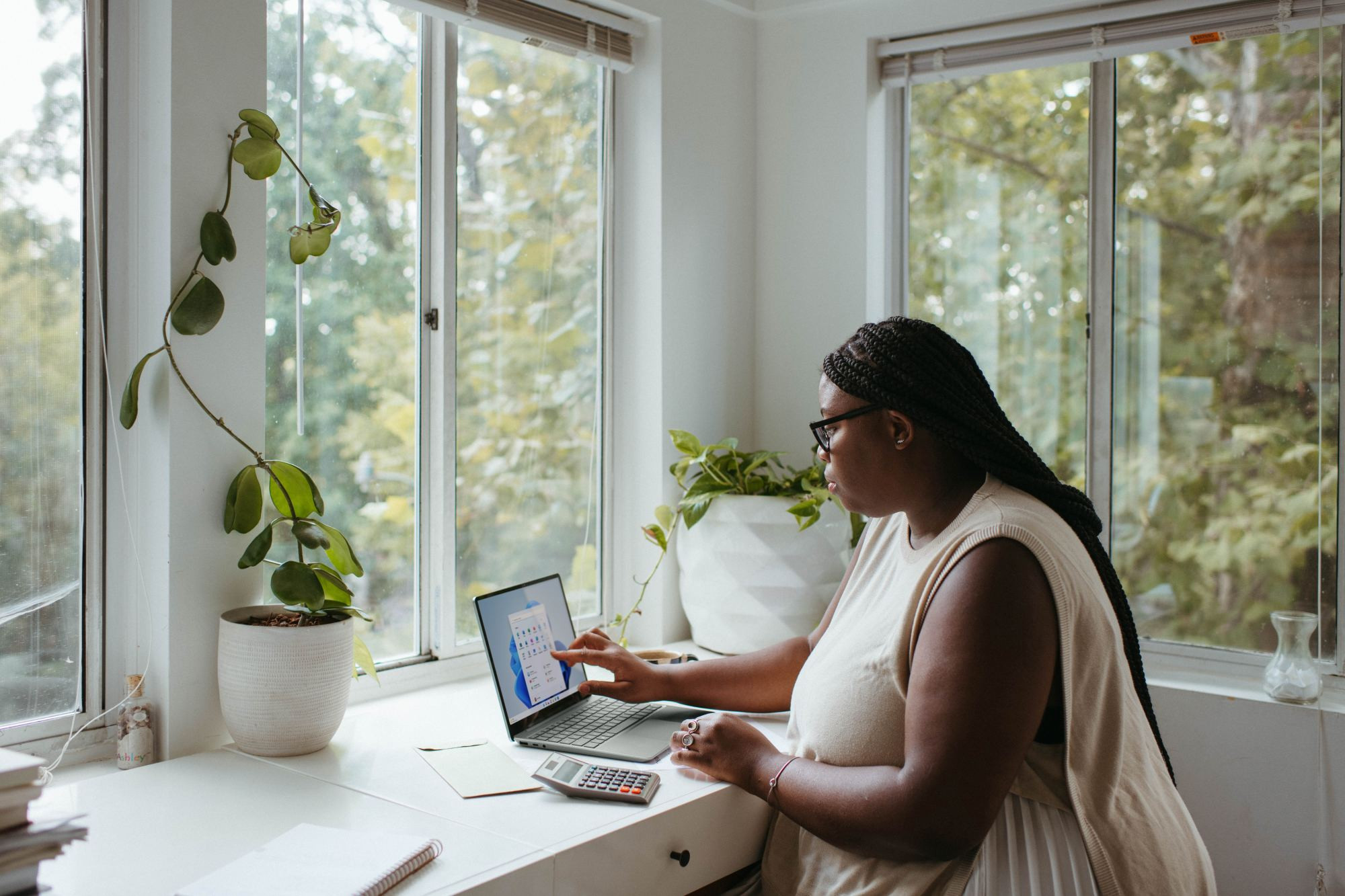 Woman working on her laptop at contemporary desk with lovely house plants and greenery outside